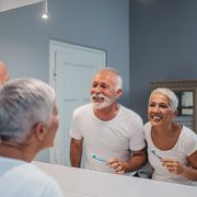 A senior citizen couple brushes their teeth together.