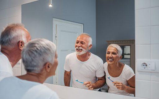 A senior citizen couple brushes their teeth together.