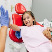 A young girl gives her dentist a high five while sitting in the exam chair following her dental appointment.