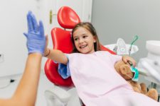 A young girl gives her dentist a high five while sitting in the exam chair following her dental appointment.